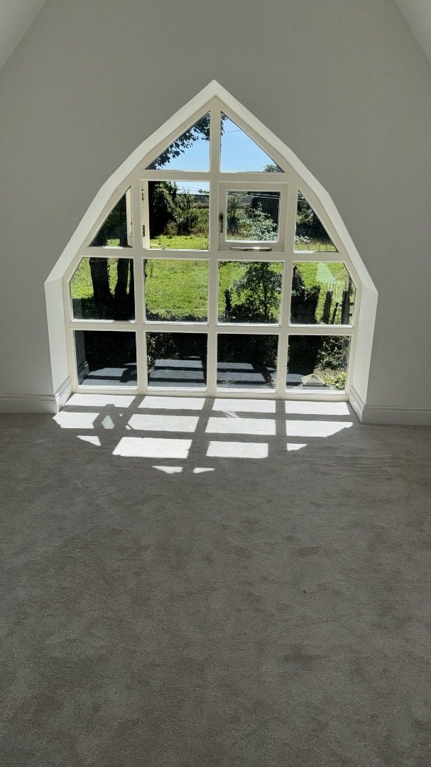 Pointed arched window at the end of a finished carpeted room, looking out to the garden