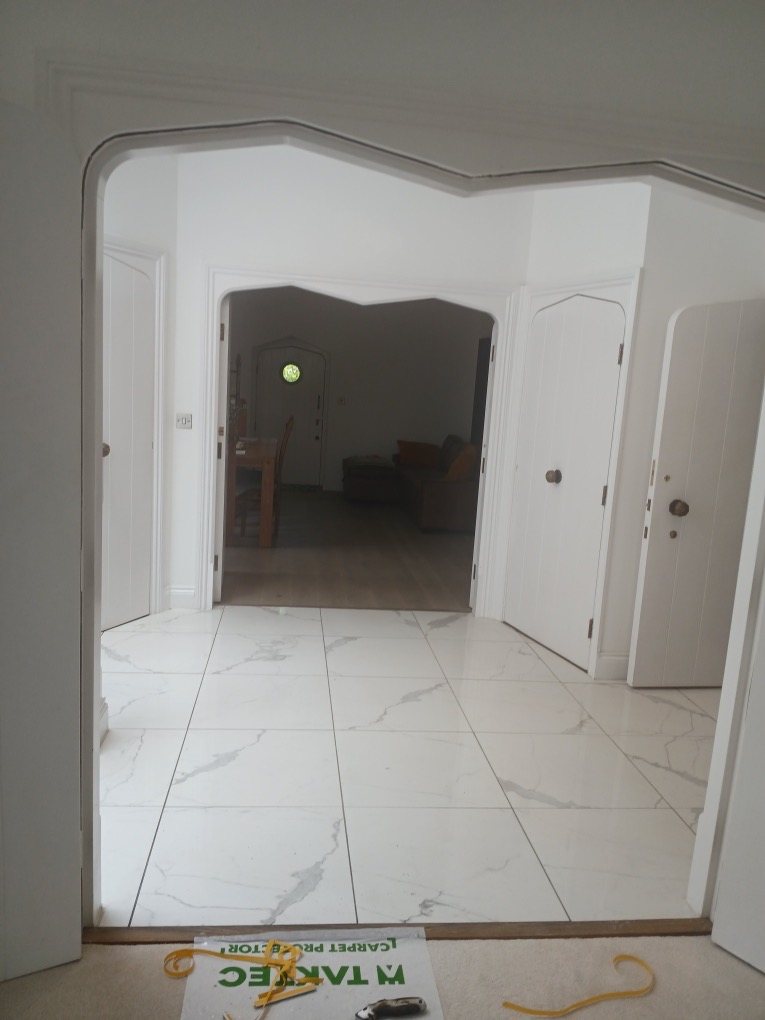 Shaped archway opening onto a marble-effect tiled hall with white plank doors