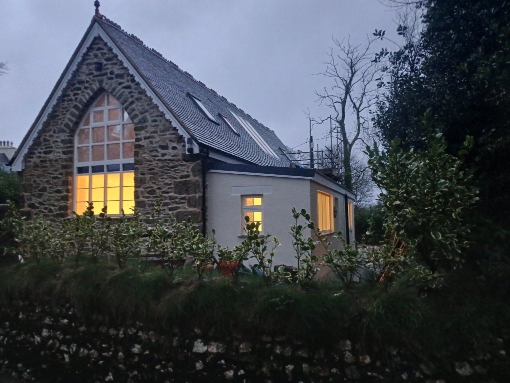 Stone gable with the arched window lit at dusk, beside a white-walled side wing