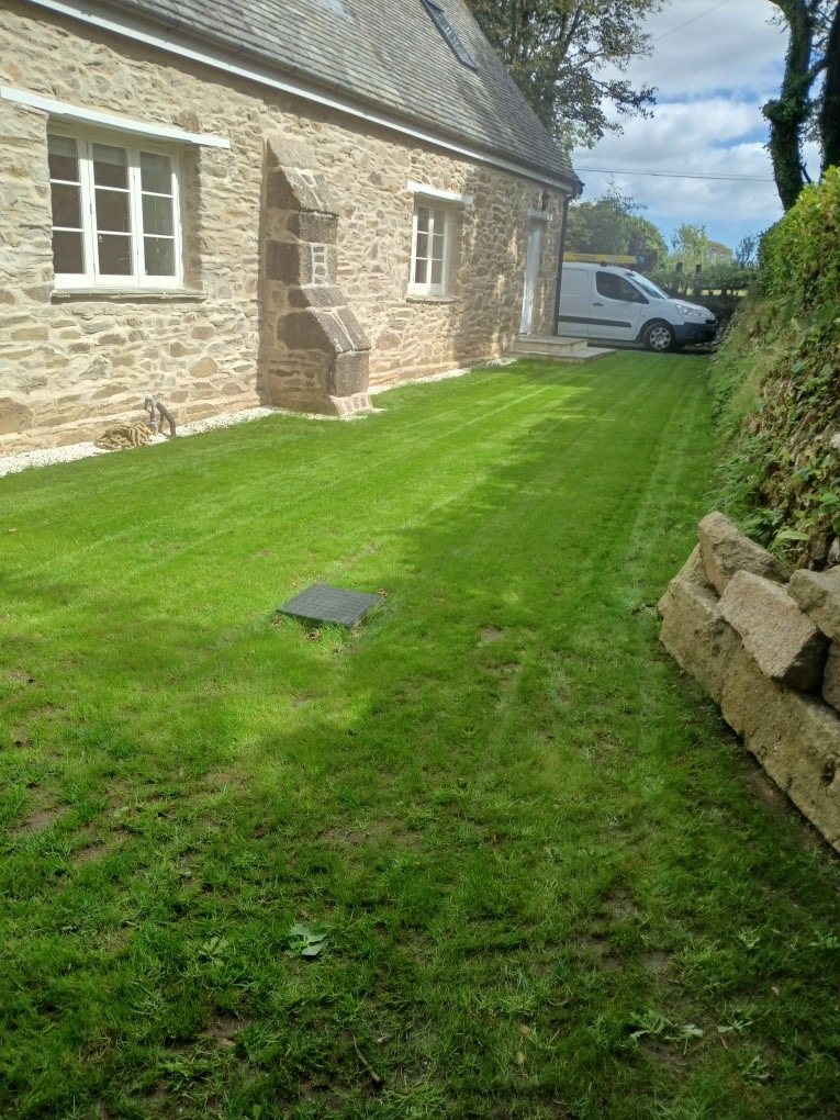 Restored stone side wall with white windows beside a newly laid lawn