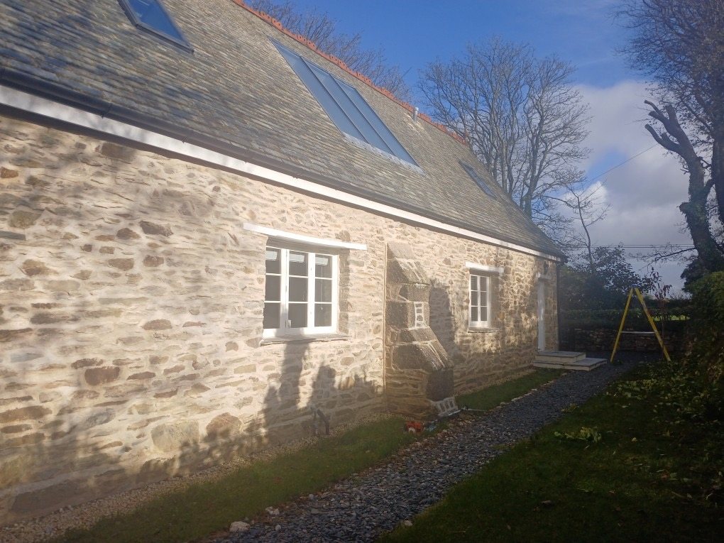 Side wall of the restored stone building with white windows and a slate roof with roof glazing