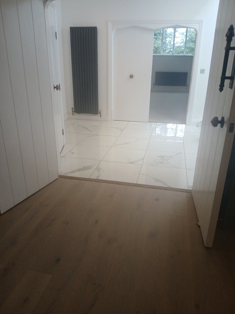 Oak floor leading to a marble-effect tiled hall with white plank doors and a black radiator