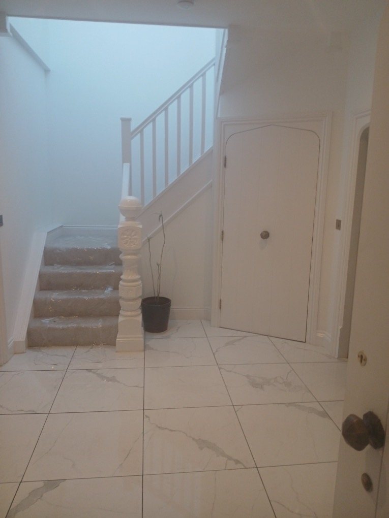 Tiled hallway with a white staircase and an arched cupboard door