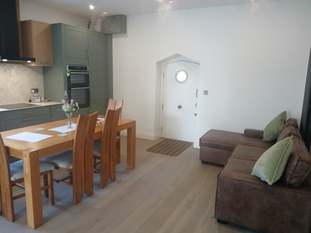 Kitchen and dining area with green units, an oak table and a corner sofa