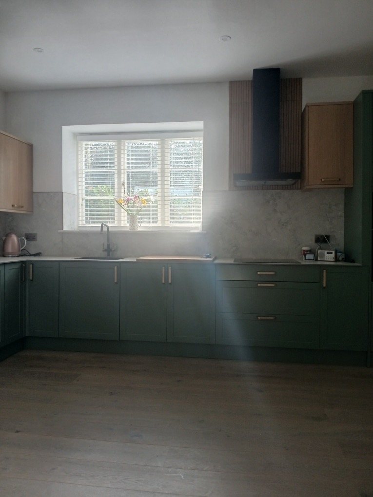 Kitchen with green shaker units, timber wall cupboards and a window over the sink