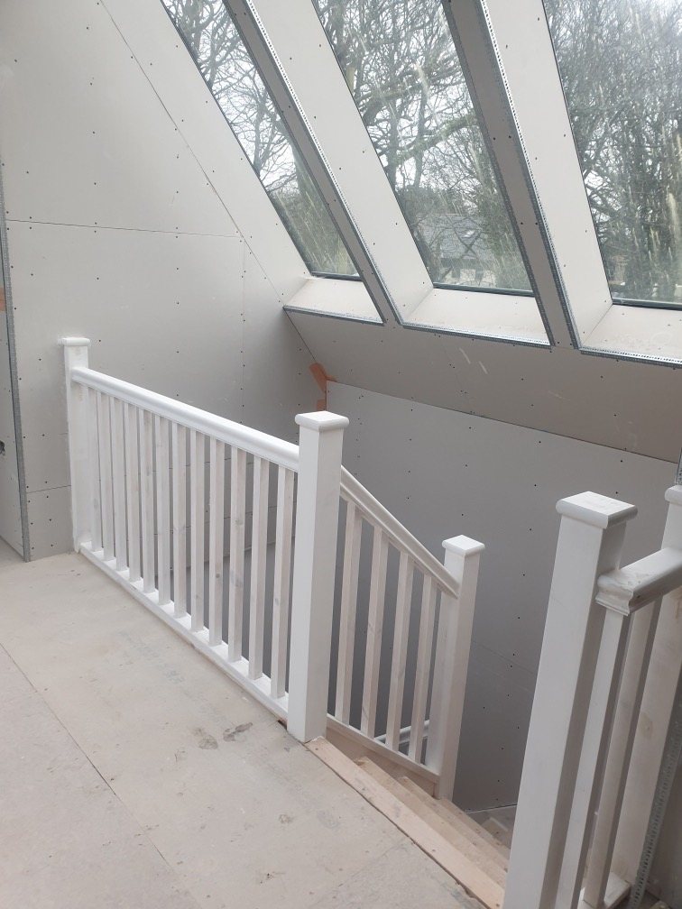 Landing with a white painted balustrade under glazed roof panels, walls boarded ready for plaster
