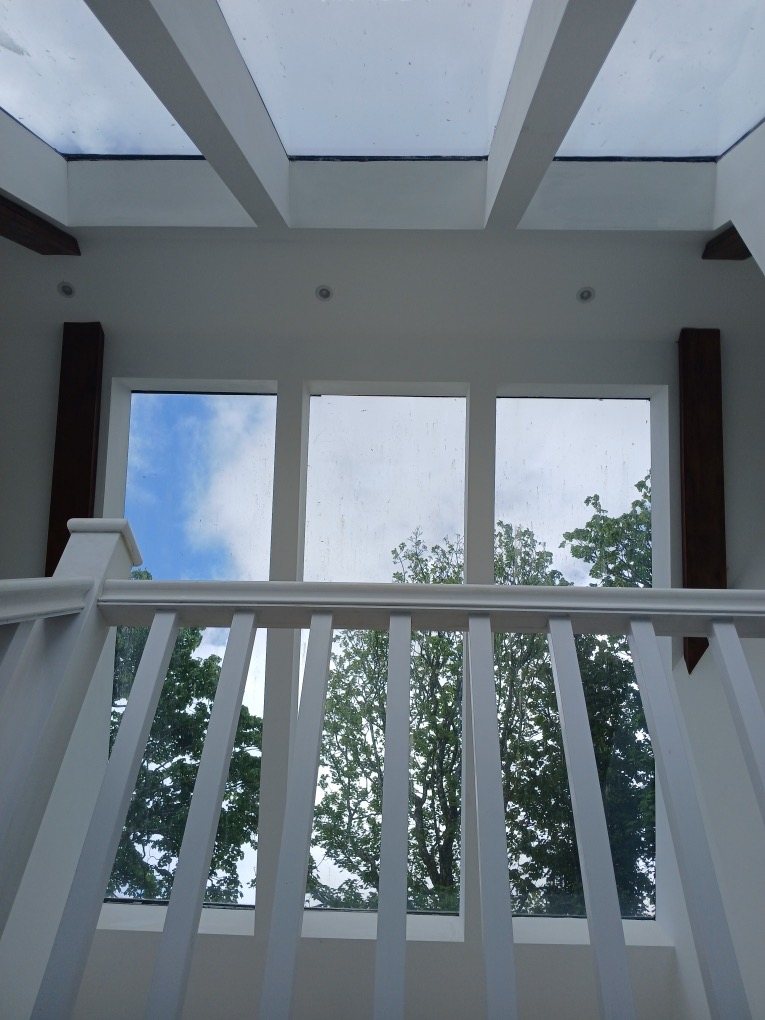 White landing balustrade in front of tall windows, under glazed roof panels and painted beams