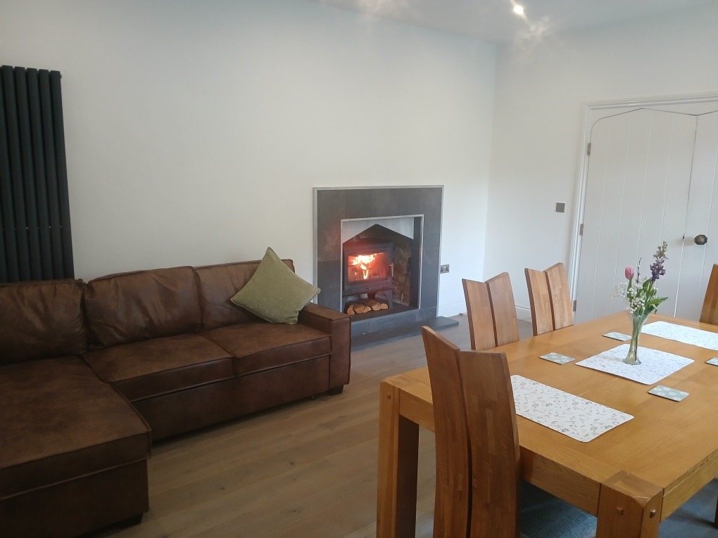 Living area with a wood-burning stove, a leather sofa and an oak dining table