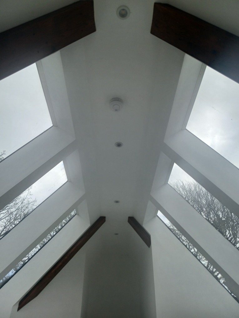 Looking up into a finished white vaulted ceiling with glazed roof panels and dark beams